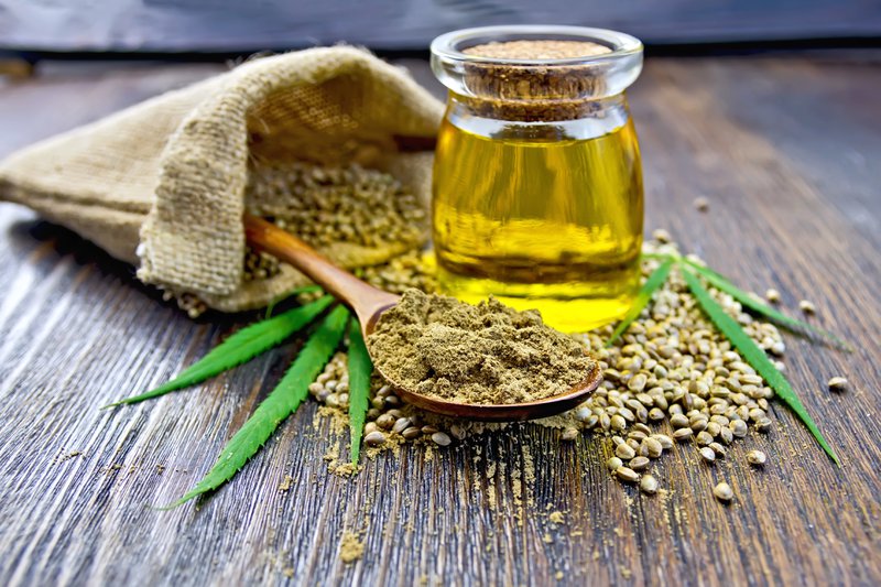 Flour hemp in a wooden spoon, hemp seed in a bag and on the table, hemp oil in a glass jar, hemp leaves on the background of wooden boards